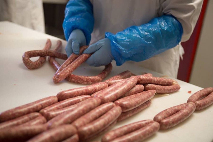man with blue plastic gloves putting fresh sausages on white table at Vavourakis Farm workshop